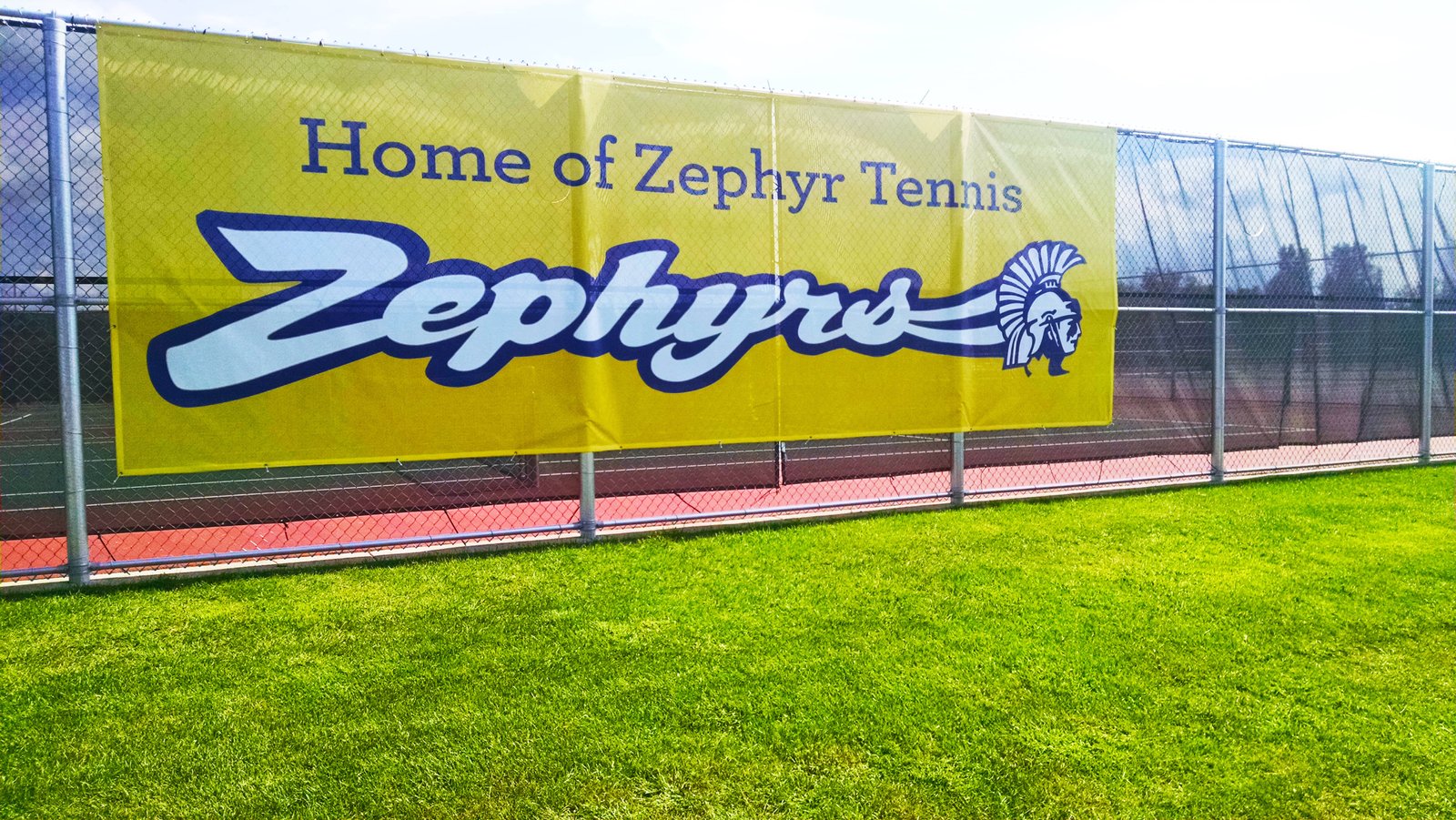 A Large Yellow Banner Hanging on a Fence Next to a Tennis Court
